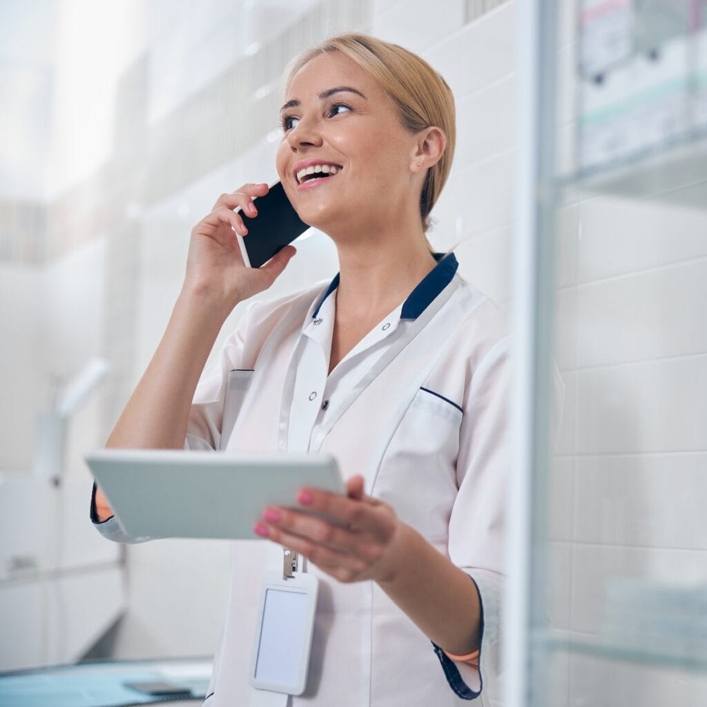 Young woman in a lab coat talks on a smartphone with patient