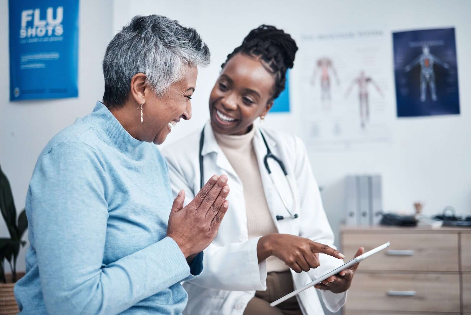 A doctor shows a tablet to a smiling older patient in an exam room